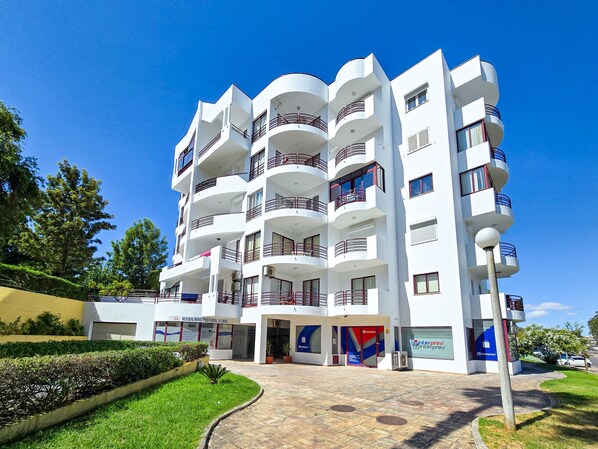 Un edificio de varios pisos con balcones, acceso pavimentado y zonas verdes.