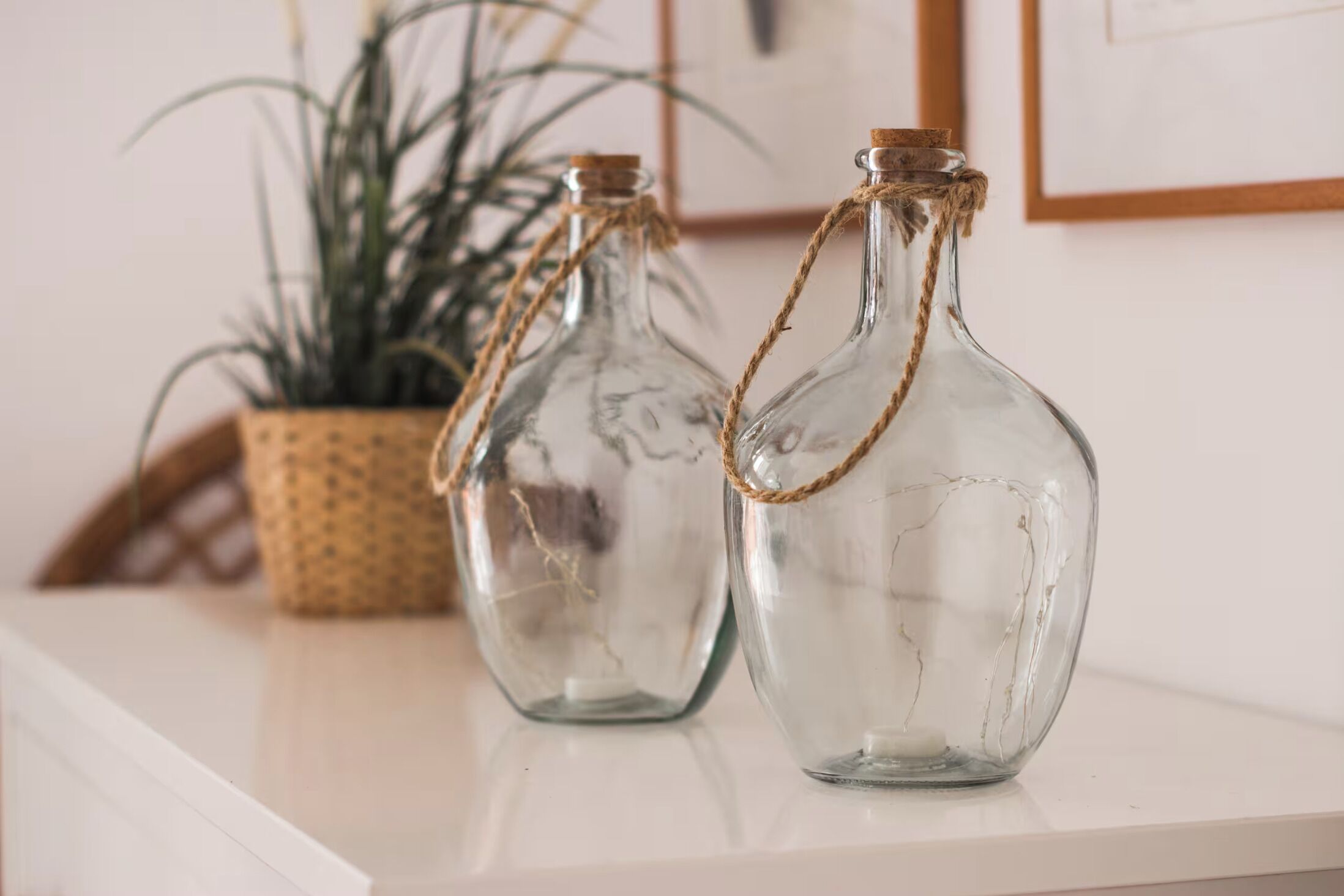 Dos botellas de vidrio transparente con tapones de corcho y cuerda, sobre una superficie blanca.