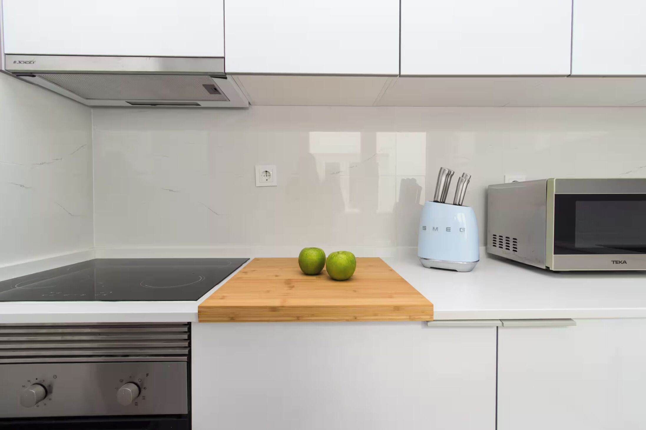 Une cuisine équipée d’un four à micro-ondes, d’une planche à découper avec des pommes et d’un porte-couteaux.