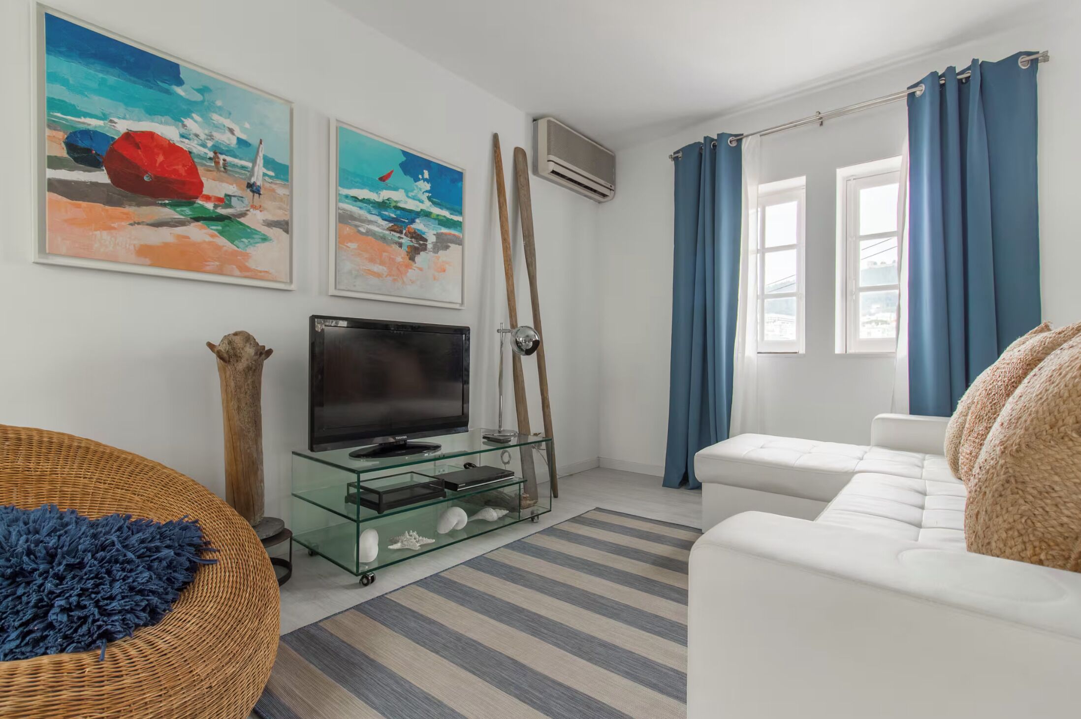 Una sala de estar con televisor, un aparador de vidrio, un sofá blanco y un tapete a rayas.