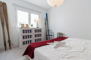 A bedroom with a bed, a window, a white dresser, a lamp, and a chair. - Corema Apartment, Sesimbra, Setúbal (Sesimbra)