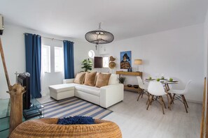 A modern living room with a white sofa, a dining table with chairs, and a large window with blue curtains. - Corema Apartment, Sesimbra, Setúbal (Sesimbra)