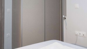 Hotellihuone, jossa on sänky, vaatekaappi ja pistorasia seinässä.