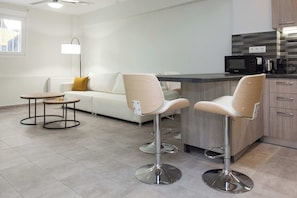 Eine moderne Küche mit Barbereich, zwei Barhocker, einer Couch, einem kleinen runden Tisch und einer Stehlampe.