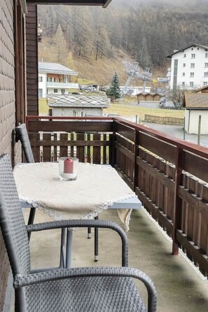 A balcony with a table and chairs, overlooking a residential area with houses and a ski lift in the background. - Bergfreude Appartement/Fewo 4-Bettwohnung by Interhome (Saas-Grund)
