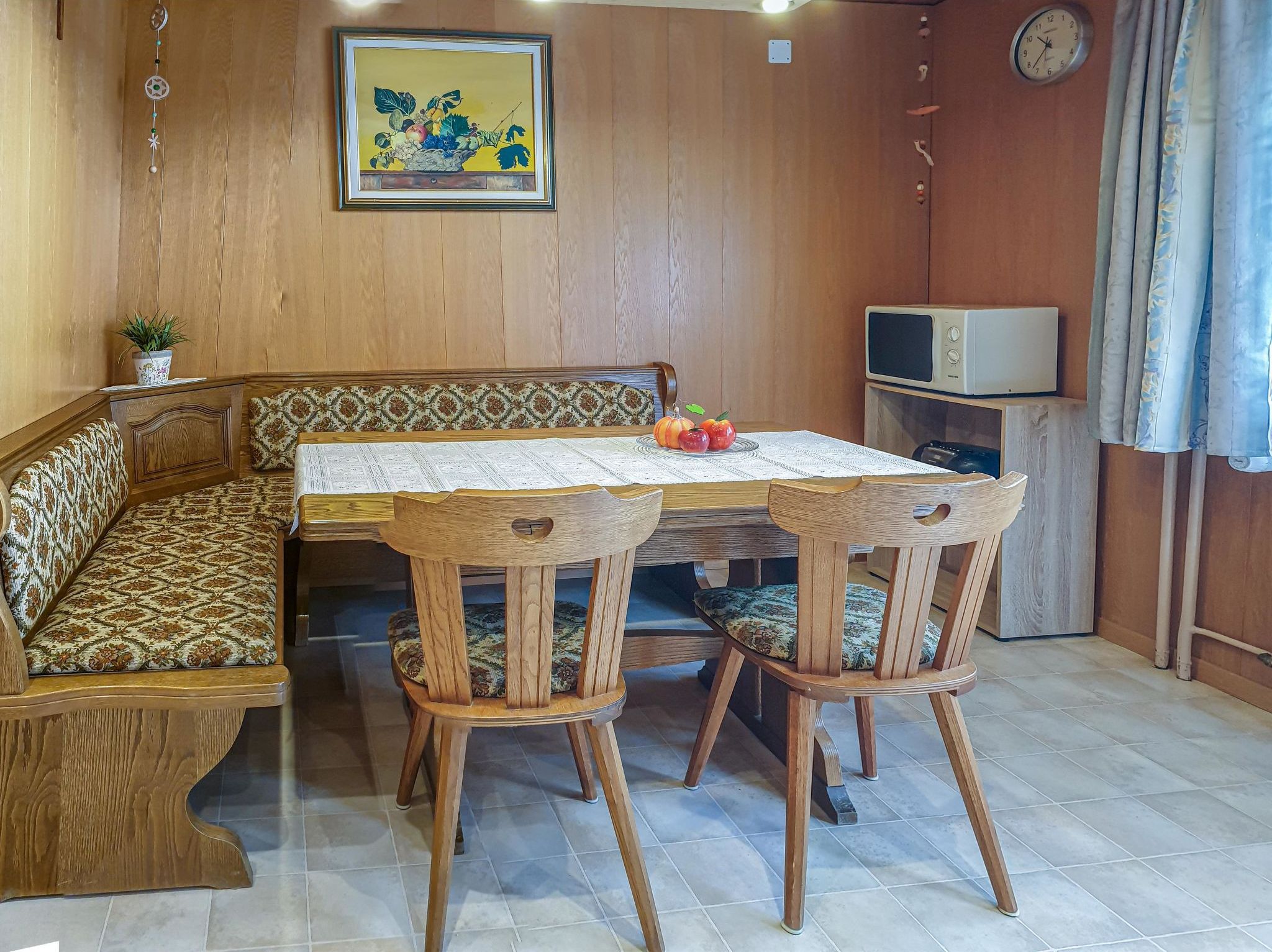 A wooden dining area with a bench and table, a clock, and a television on a shelf.