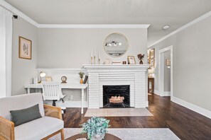 Ein Wohnzimmer mit weißem Kamin, einem weißen Sofa, einem Couchtisch mit Pflanze sowie einem Essbereich mit Tisch und Stühlen.