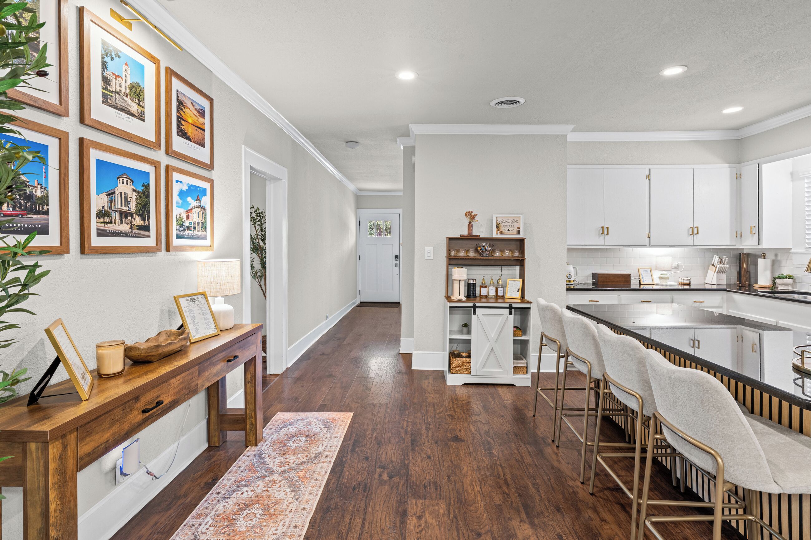 A modern kitchen with white cabinetry, a central island with bar stools, and a dining area with a patterned rug.