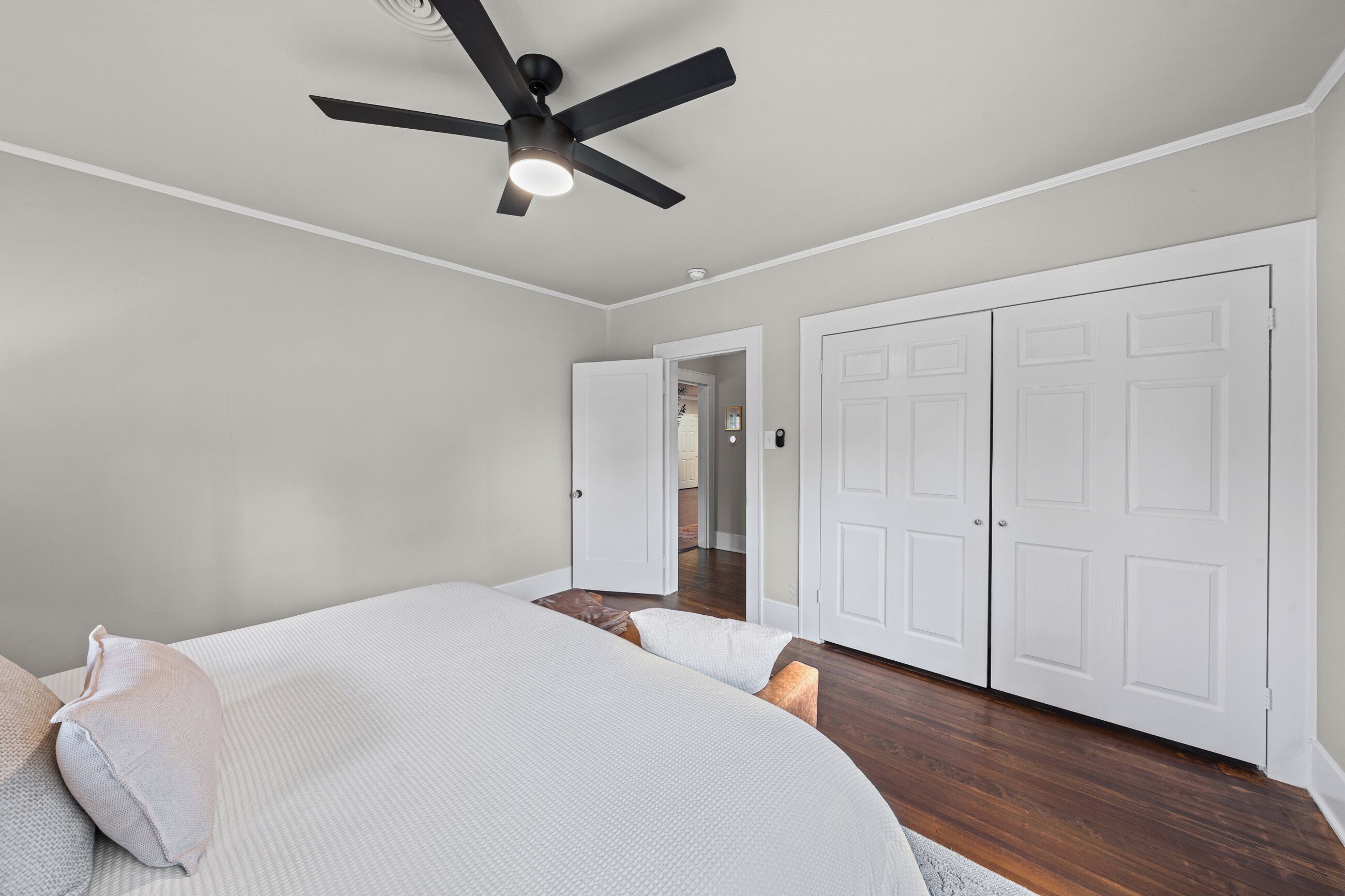 A bedroom with a bed, a ceiling fan, and white double doors.