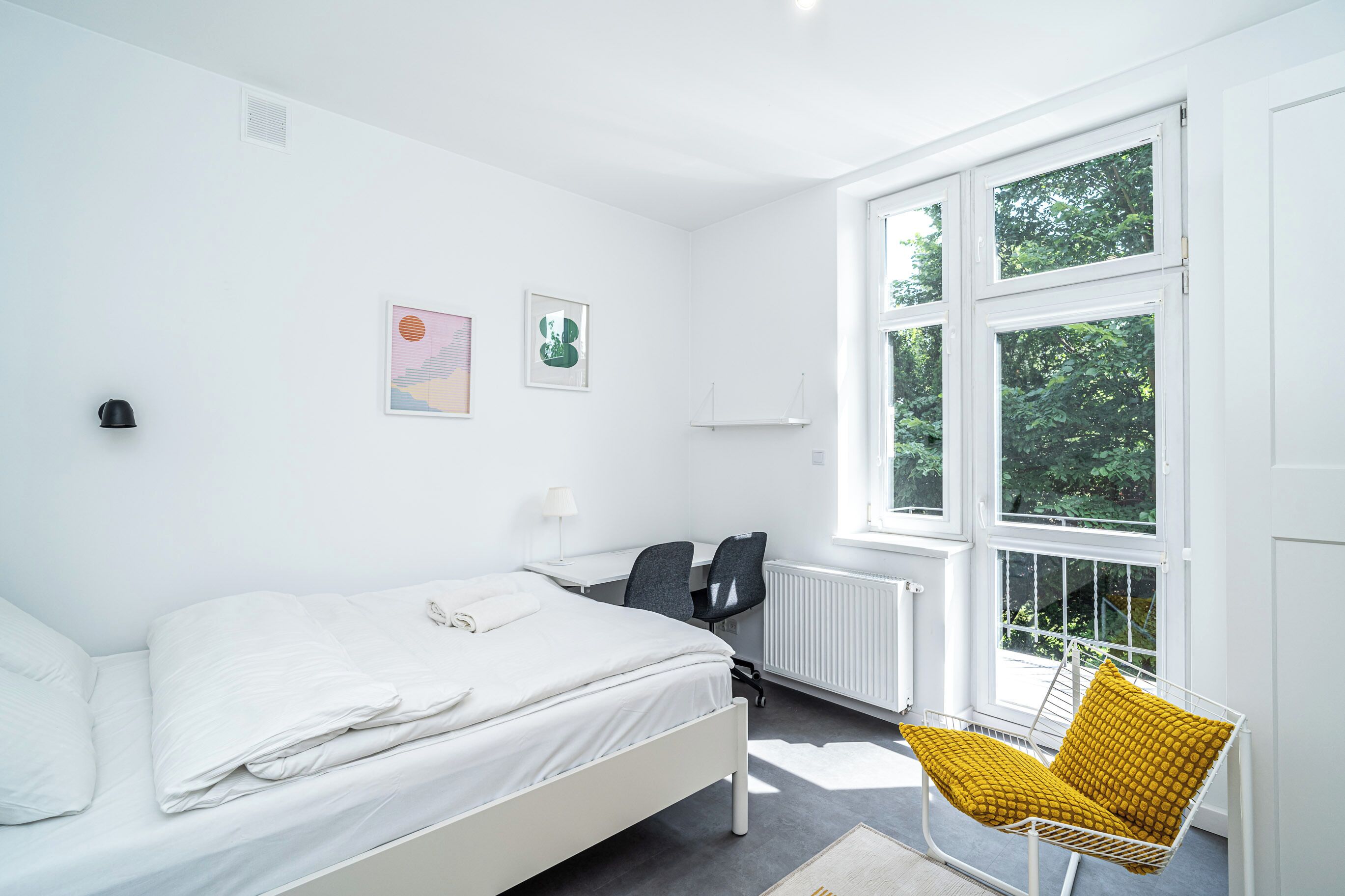 Un dormitorio moderno con cama, escritorio, silla y un amplio ventanal.