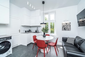 Una cocina moderna con armarios blancos, un comedor con sillas rojas, un sofá negro y una obra de arte con temática de cebra.