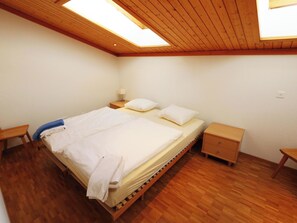 Ein Schlafzimmer mit einem hölzernen Bett, zwei Nachttischen, einem kleinen Tisch und einem Oberlicht.