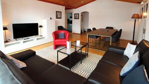 A modern living room with a flat-screen TV, red sofa, black leather couches, a dining table with chairs, and a kitchen in the background. - Cristal Appartement/Fewo 6-Bettwohnung Nr. 25 by Interhome (Saas-Fee)