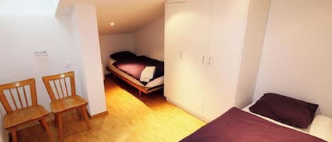 A compact bedroom with a bed, a wardrobe, a desk with chairs, and a small window.