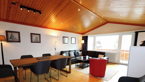 A modern interior with a wooden ceiling, a dining area with a table and chairs, a sofa, and a red ottoman. - Cristal Appartement/Fewo 6-Bettwohnung Nr. 25 by Interhome (Saas-Fee)