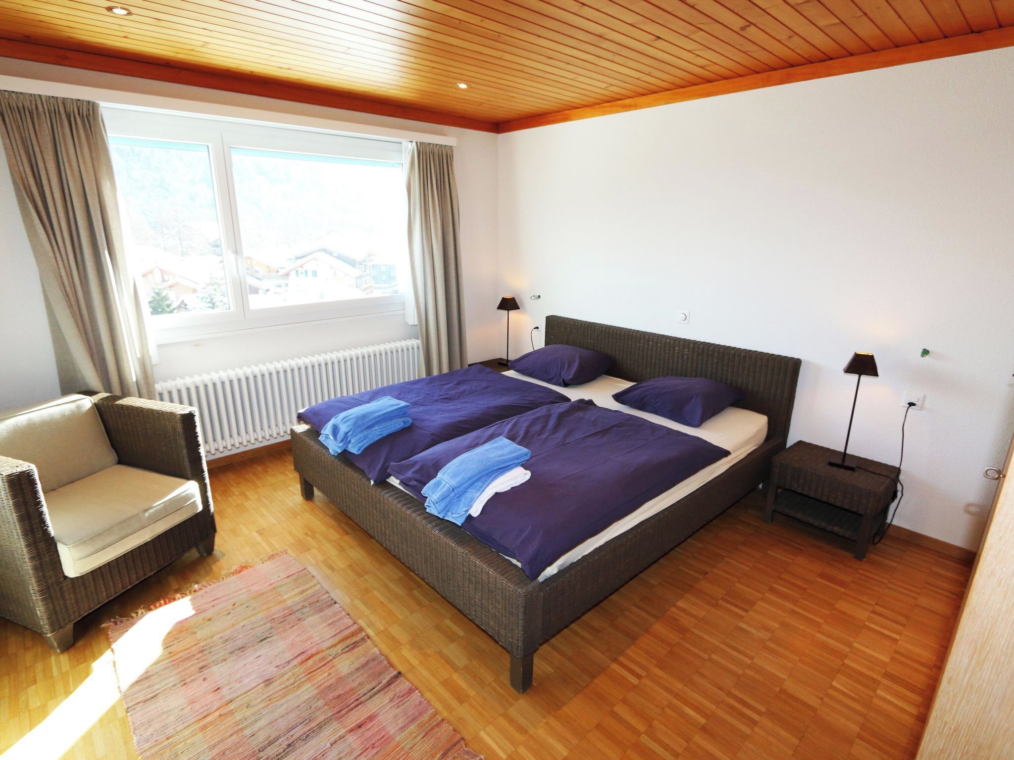 A bedroom with a large bed, a chair, a nightstand, and a window with curtains.