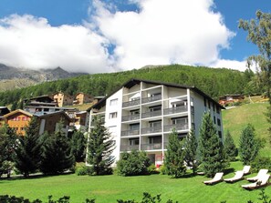 Ein mehrgeschossiges Hotel mit Balkonen, umgeben von Grünflächen und Bergen.
