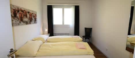 A room with two beds, a radiator, a window with curtains, and a painting on the wall.