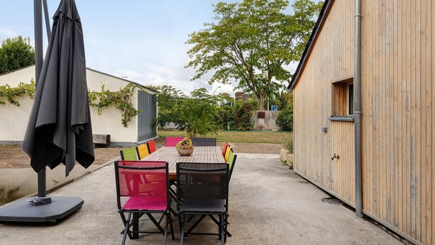 Eine Terrasse im Freien mit Tisch und Stühlen, einer überdachten Lounge-Ecke und einem Holzgebäude.