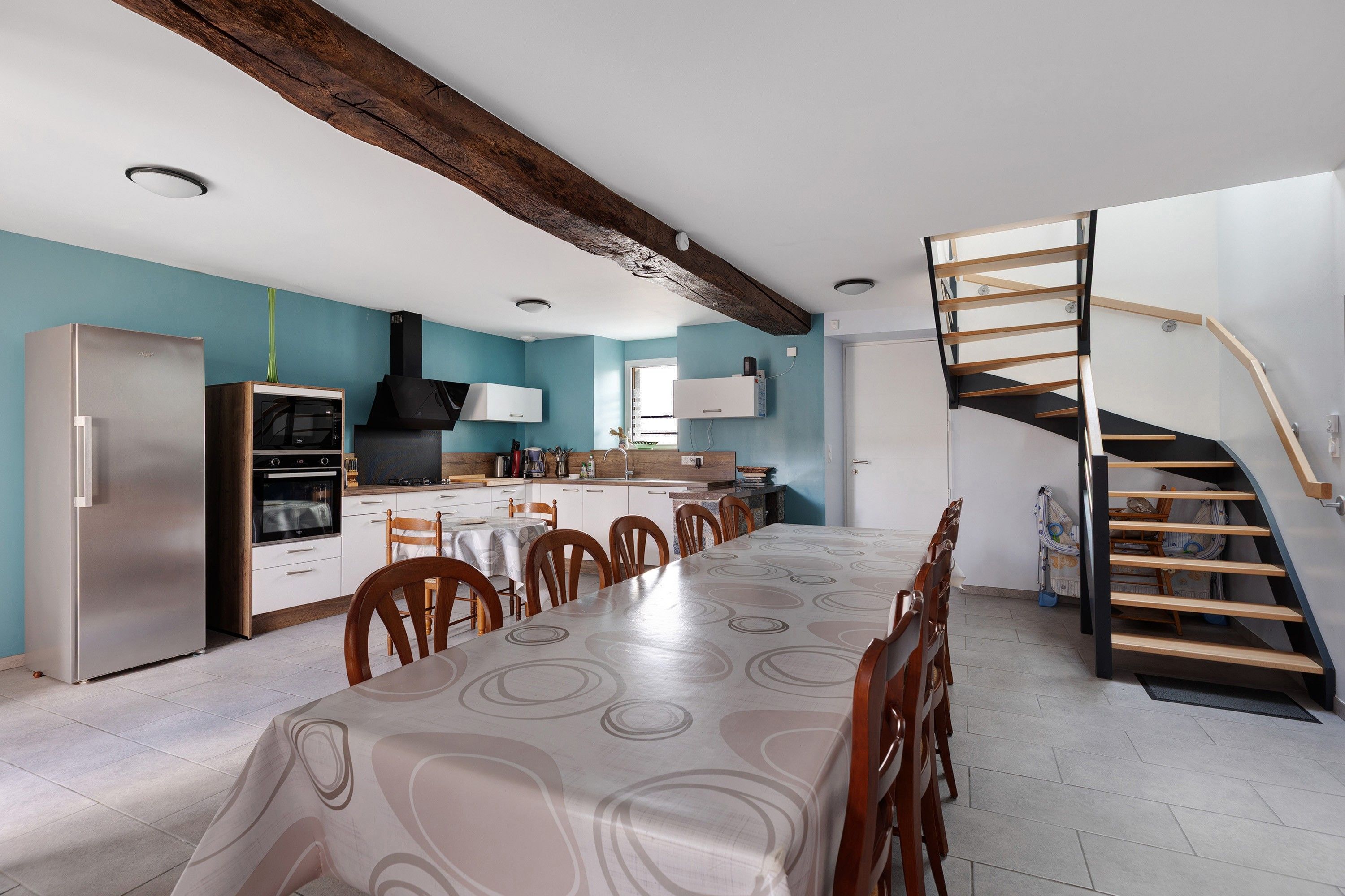 A modern kitchen with a dining area, featuring a built-in oven, microwave, and a wooden staircase.