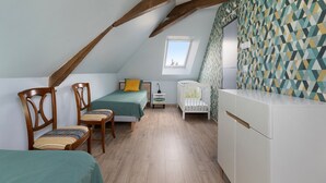 Ein gemütliches Schlafzimmer im Dachgeschoss mit schrägen Wänden, einem Holzstuhl, einem Bett, einem Babybett und einer Wand mit Muster.