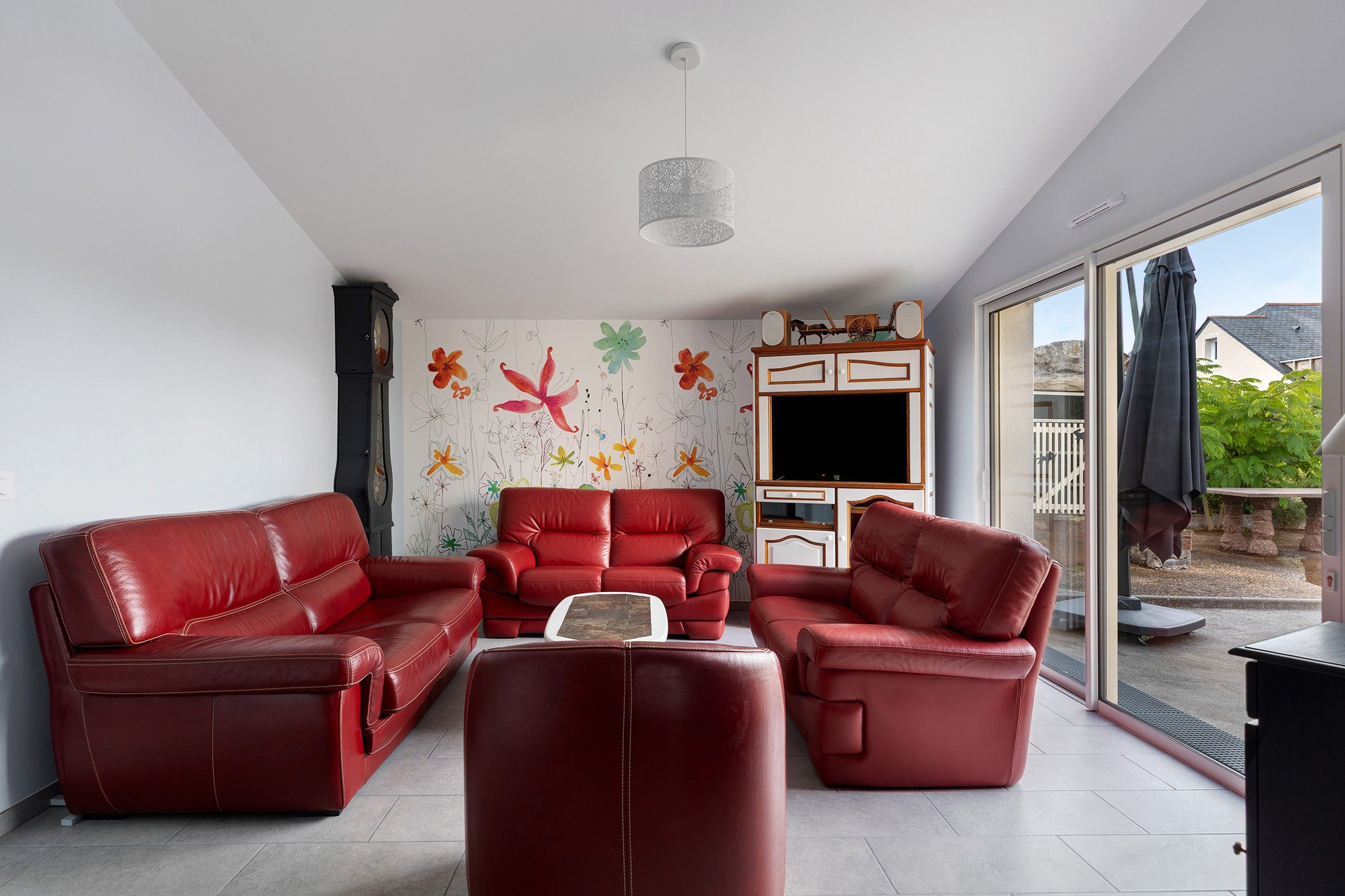 A living room with a red leather sofa set, a flat-screen TV, and a decorative wall with floral patterns.