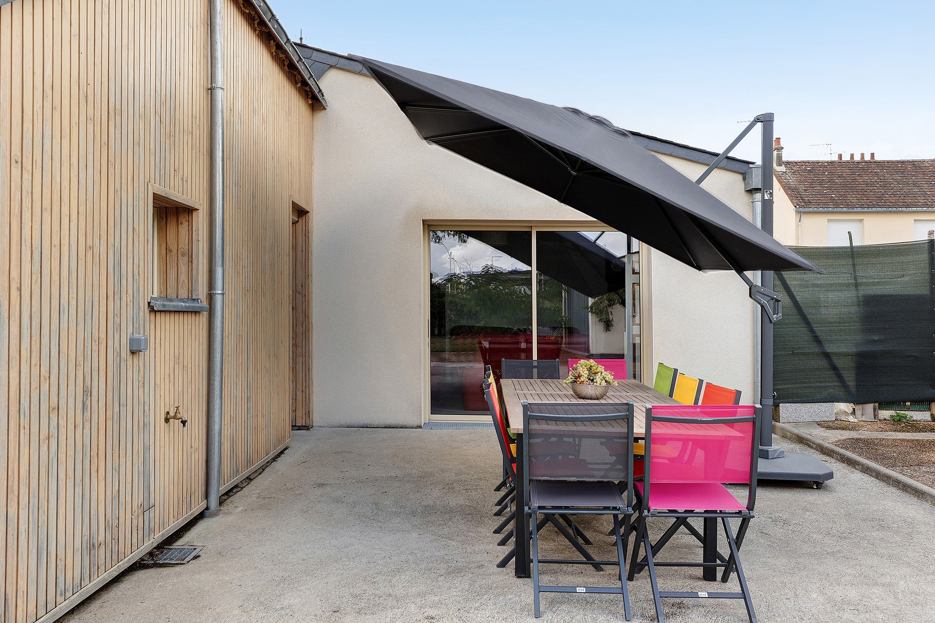 A patio area with a table and chairs, a black umbrella, and a building with a wooden facade.