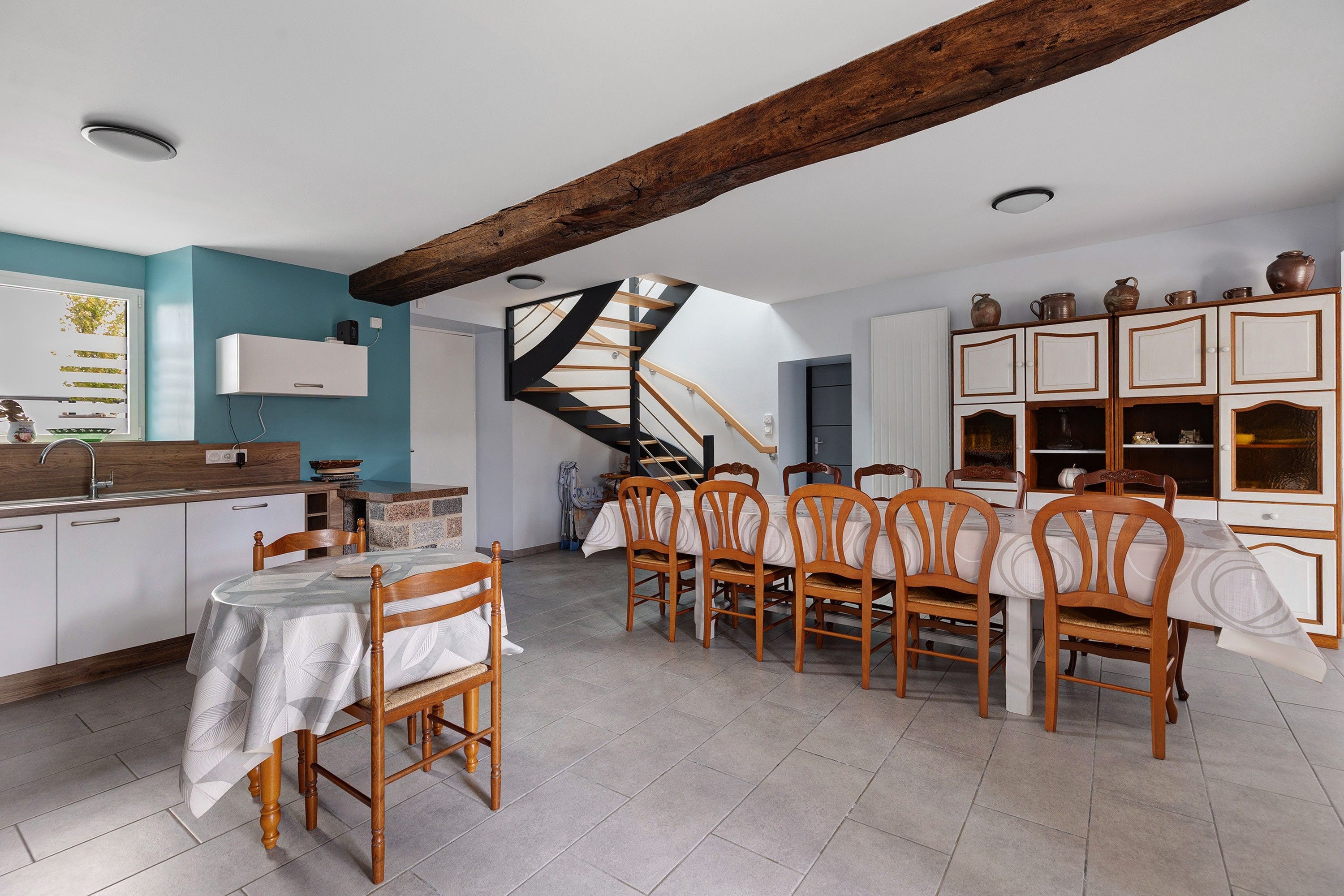 A dining area with a wooden table and chairs, a kitchen with white cabinets, and a spiral staircase.