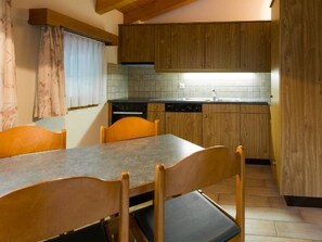 A compact kitchen with wooden cabinets, a tiled backsplash, and a dining table with chairs. - Haus Evita Appartement/Fewo 4-Bettwohnung Nr. 60 by Interhome (Saas-Grund)