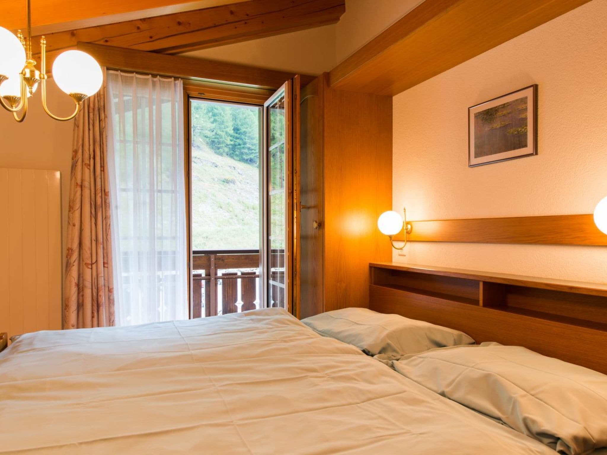 A bedroom with a bed, wooden headboard, a window with curtains, and a wall-mounted light fixture.