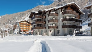 A multi-story hotel with balconies, a ski slope in the foreground, and a mountainous backdrop. - Haus Evita Appartement/Fewo 4-Bettwohnung Nr. 60 by Interhome (Saas-Grund)