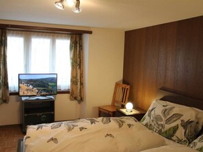 Ein Schlafzimmer mit einem Bett, einem Fernseher, einem Sessel und einem Nachttisch mit einer Lampe.