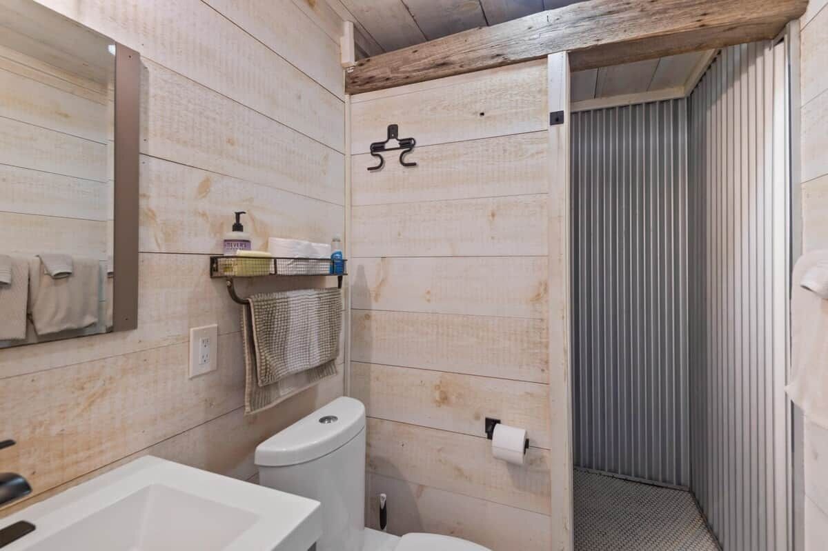 A bathroom with a wooden wall, a toilet, a sink, and a shower area.