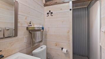 A bathroom with a wooden wall, a toilet, a sink, and a shower area.