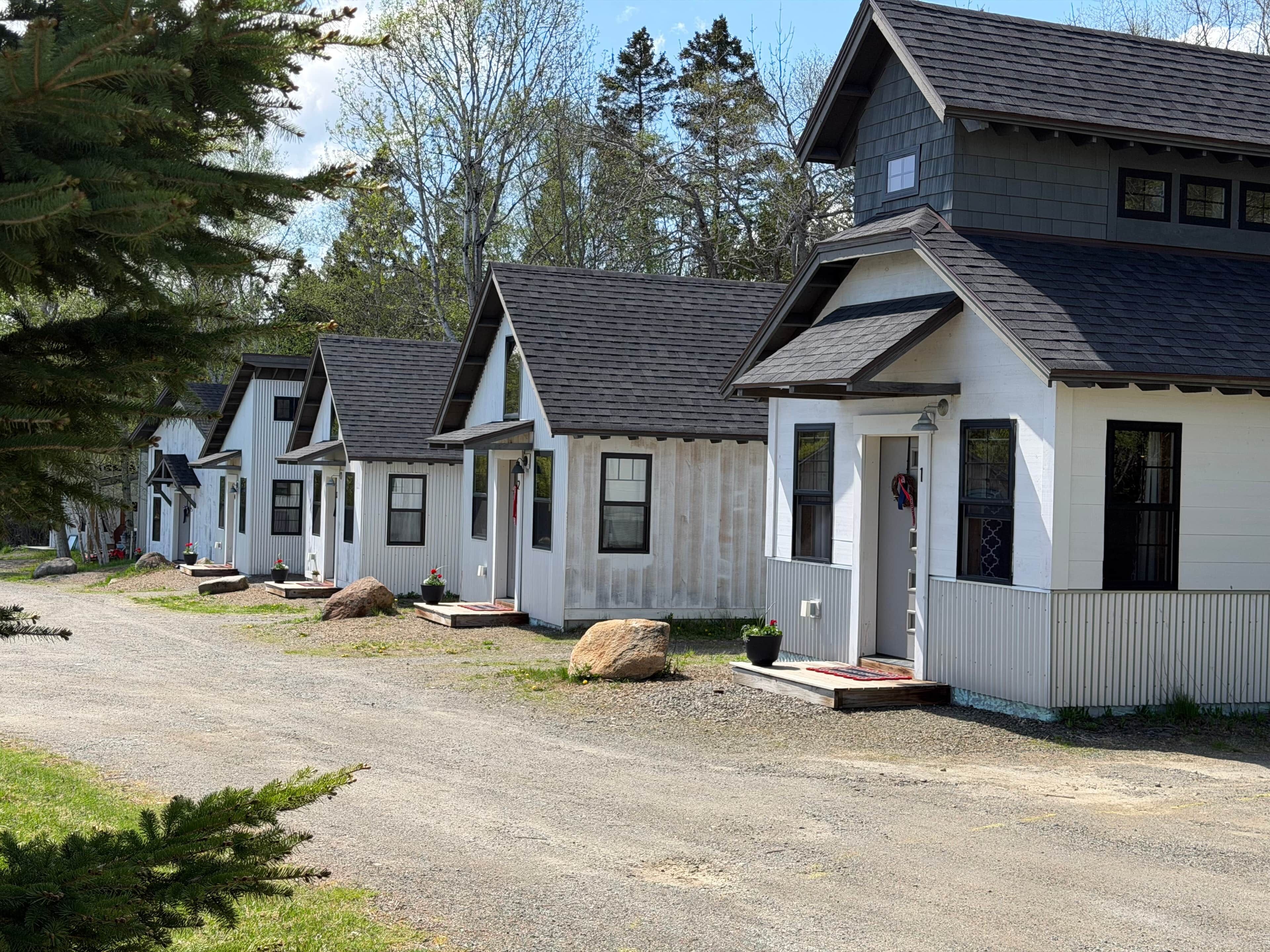 A row of white cabins with dark roofs, each with a porch and a small front door.