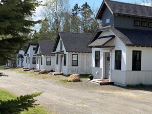 A row of white cabins with dark roofs, each with a porch and a small front door. - The Evergreen | Walk to Rangeley Lake, Sled & ATV Access (Rangeley)