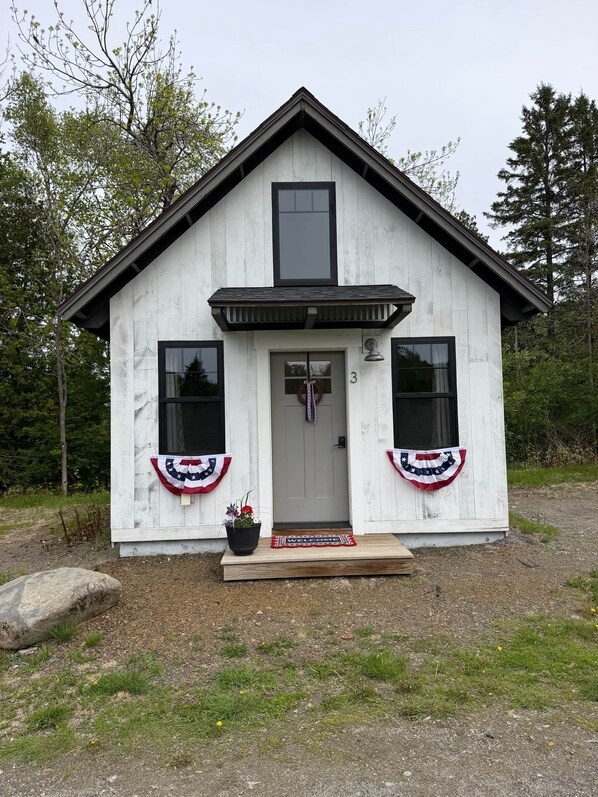 A small, single-story building with a gabled roof, a front door, and two windows on either side.