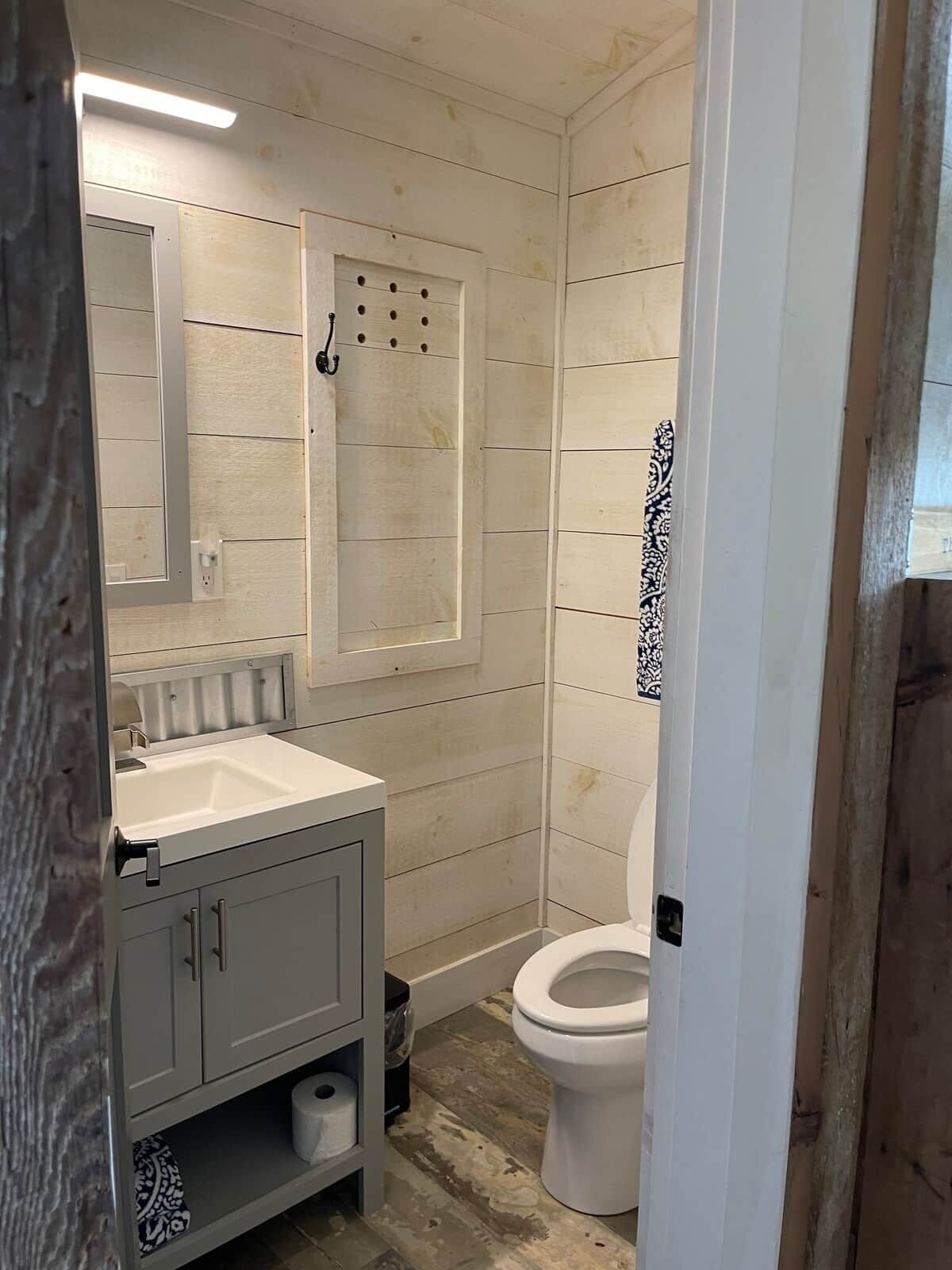 Et badeværelse med hvid vask, spejl og toilet.
