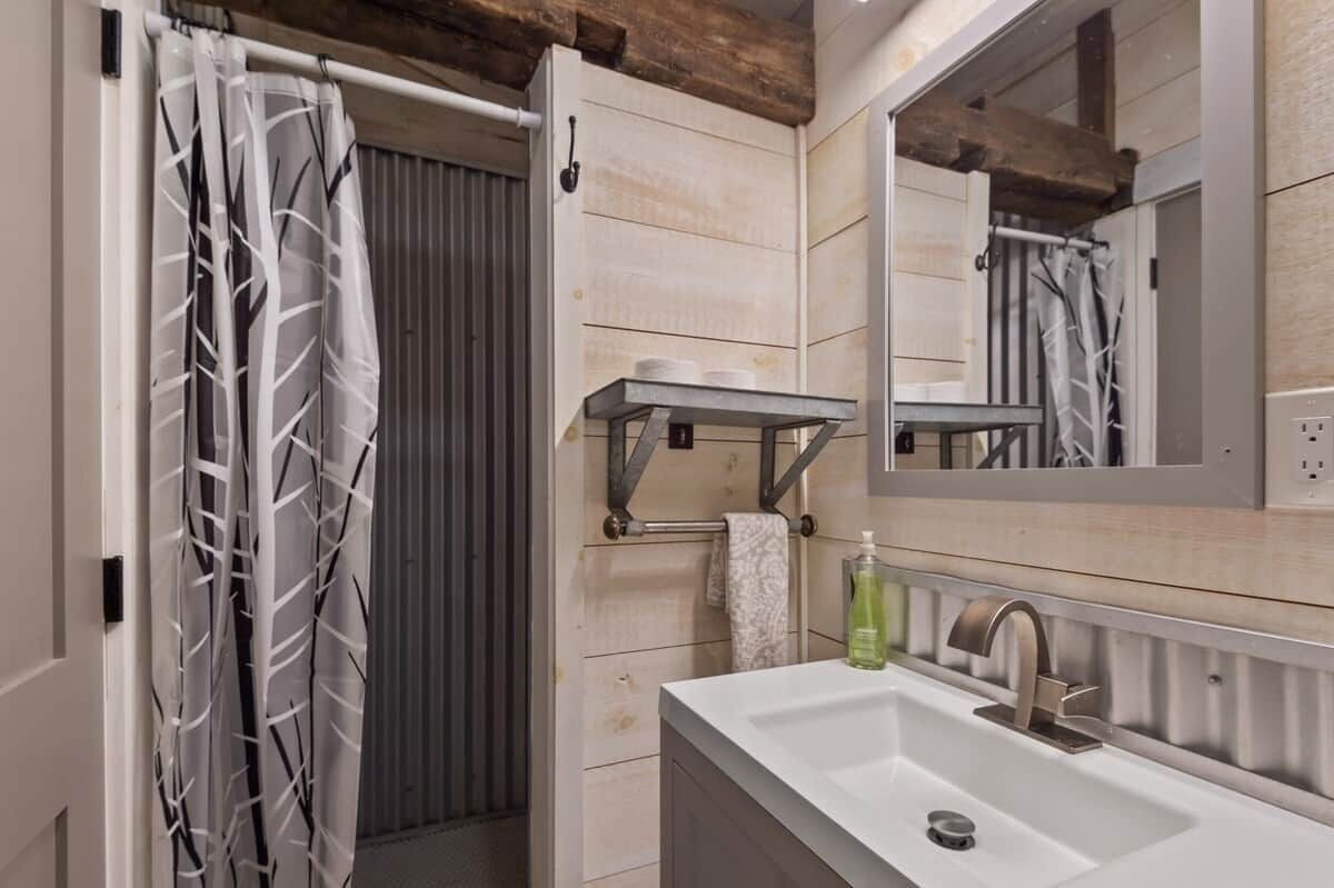 A bathroom with a shower curtain, a towel rack, a mirror, and a sink.