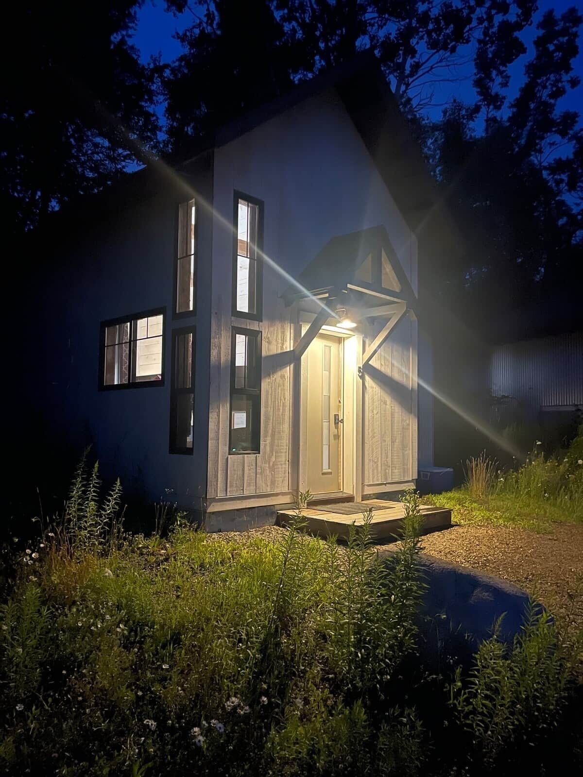 Une petite maison de plain-pied avec un porche, entourée de végétation.