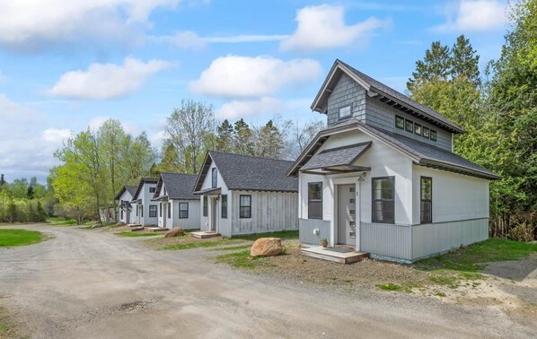 A row of single-story cabins with a gravel driveway, surrounded by trees.