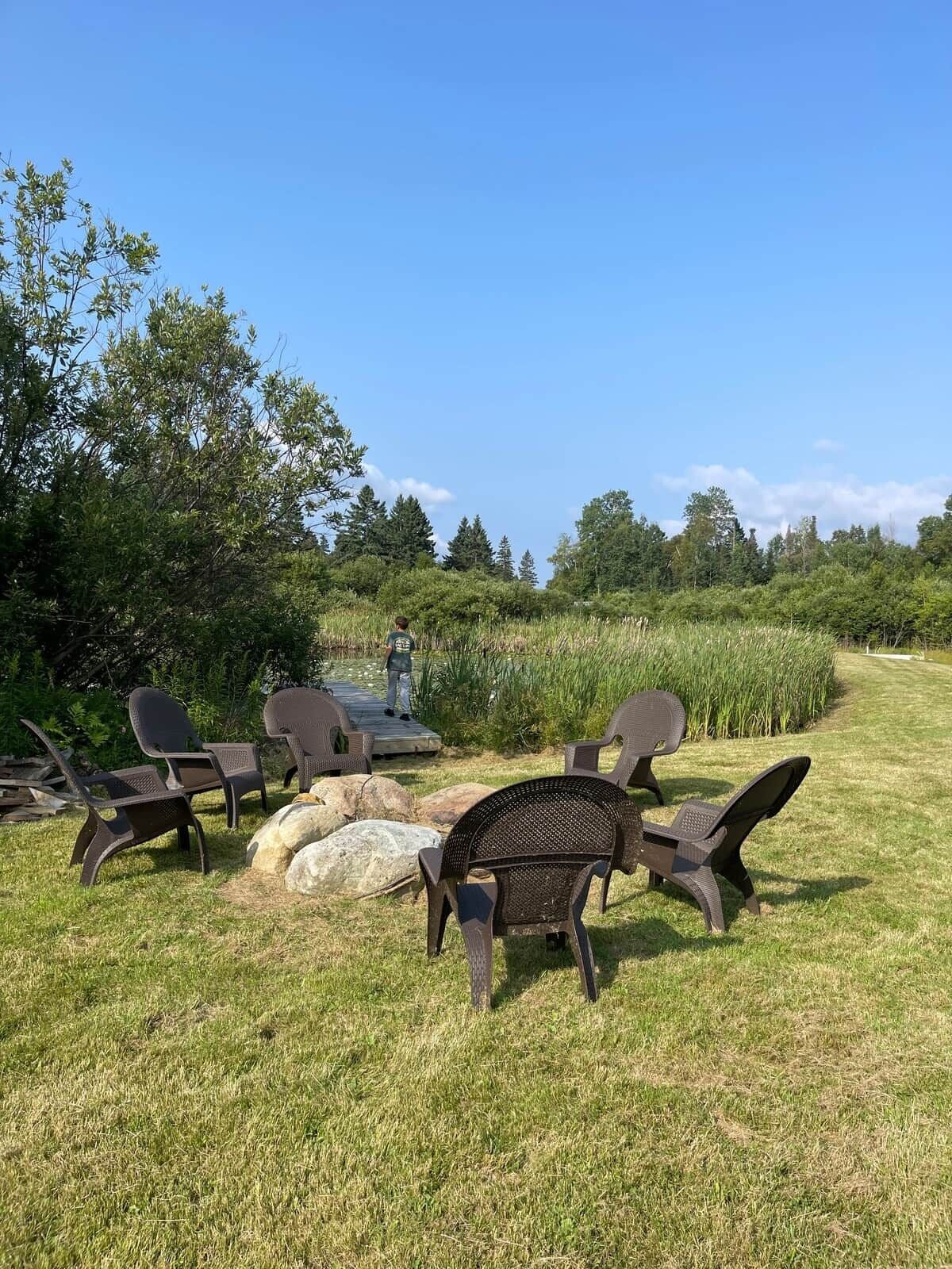 Een terras met stoelen en een tafel, omgeven door gras en bomen.