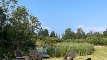 Een terras met stoelen en een tafel, omgeven door gras en bomen.