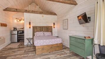 A wooden cabin interior with a bed, a green dresser, a small table, and a kitchenette.
