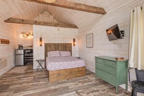 A wooden cabin interior with a bed, a green dresser, a small table, and a kitchenette.