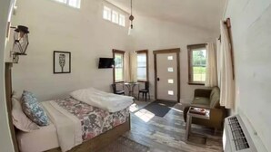 A spacious room with a bed, a small table, a chair, and a window.