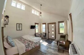 A spacious room with a bed, a small table, a chair, and a window.