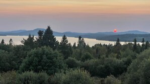 A natural landscape with a body of water, trees, and distant mountains during sunset.