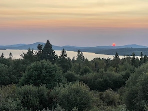 A natural landscape with a body of water, trees, and distant mountains during sunset. - The Ridgeline | Near Saddleback • Walk to Rangeley Lake (Rangeley)