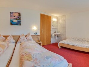 Habitación de hotel con dos camas, una puerta de madera, un baño con lavamanos y un cuadro en la pared.